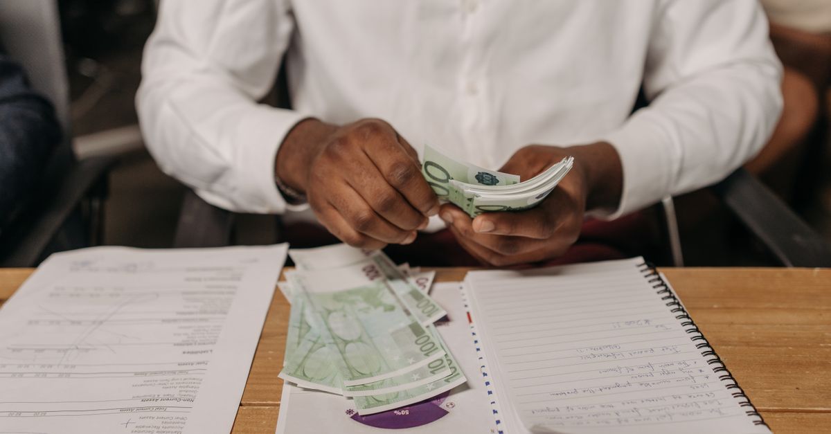 African businessman counting euro bills at a desk with documents and a notebook, highlighting finance theme.