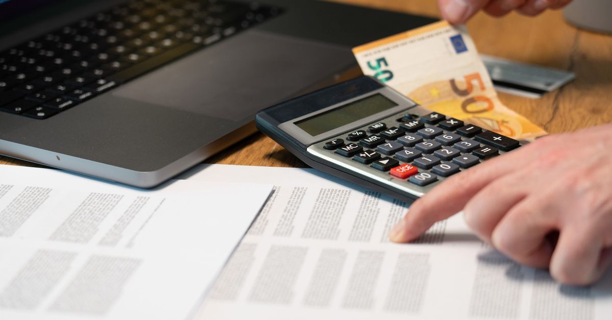 Close-up of hands using calculator with euro notes and laptop on desk.