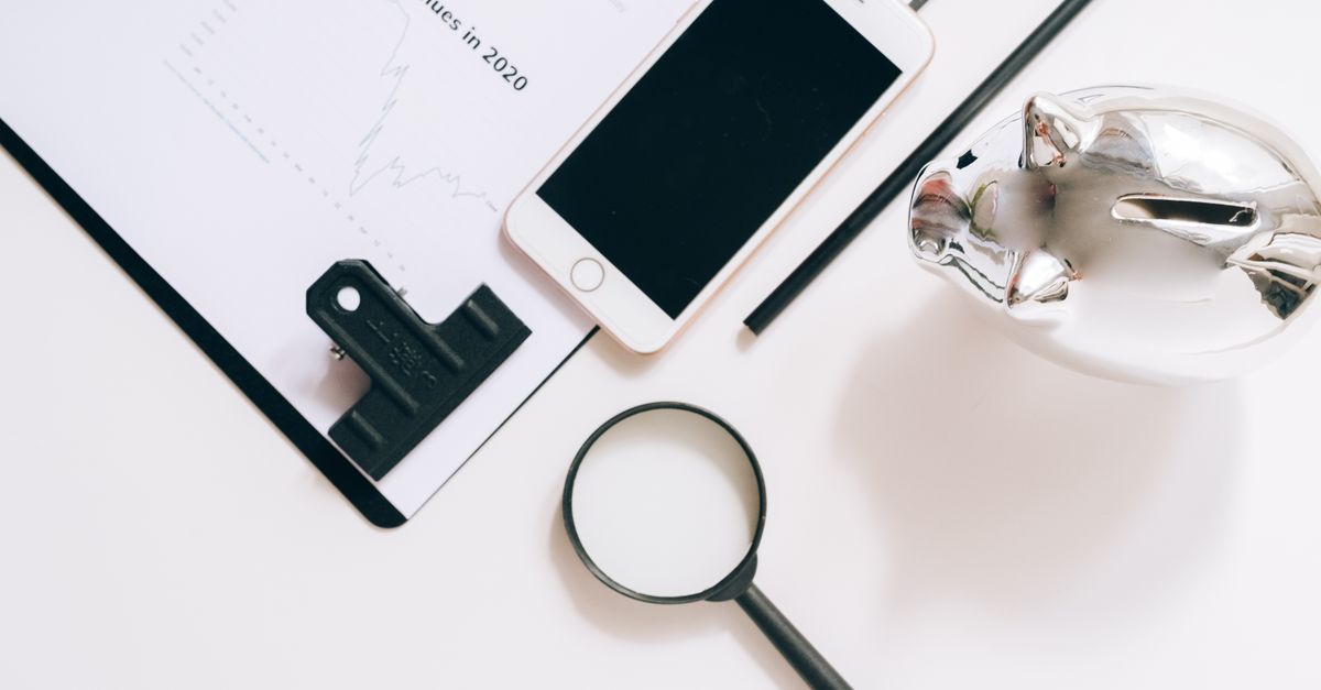 A flat lay of financial documents with a smartphone, magnifying glass, and piggy bank.