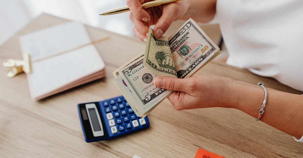 Woman counting cash with a calculator at a desk, managing finances.
