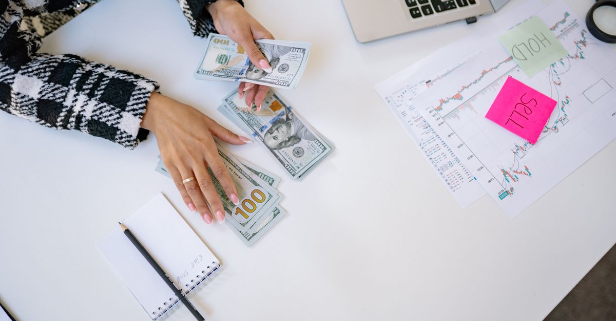 Businesswoman counting dollar bills with financial charts and laptop on table. Investment and finance concept.