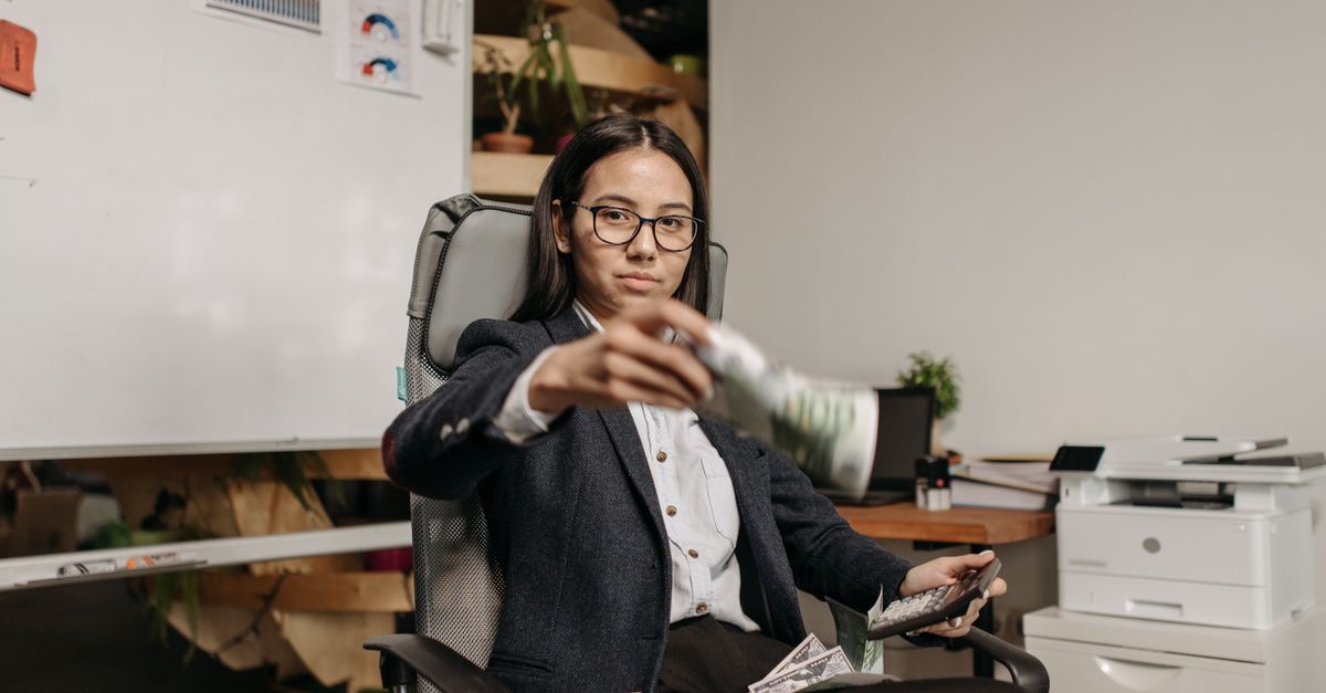 Confident businesswoman in eyeglasses counting dollar bills while sitting in a modern office.