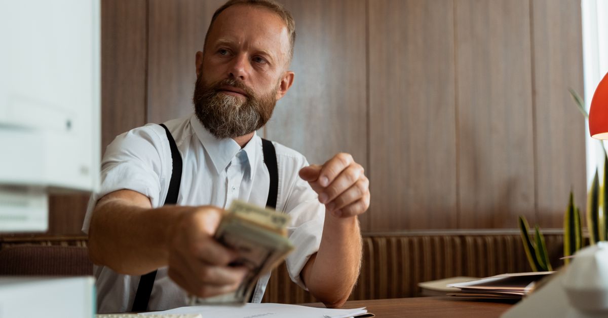 Businessman in a corporate office handling a stack of cash at his desk.