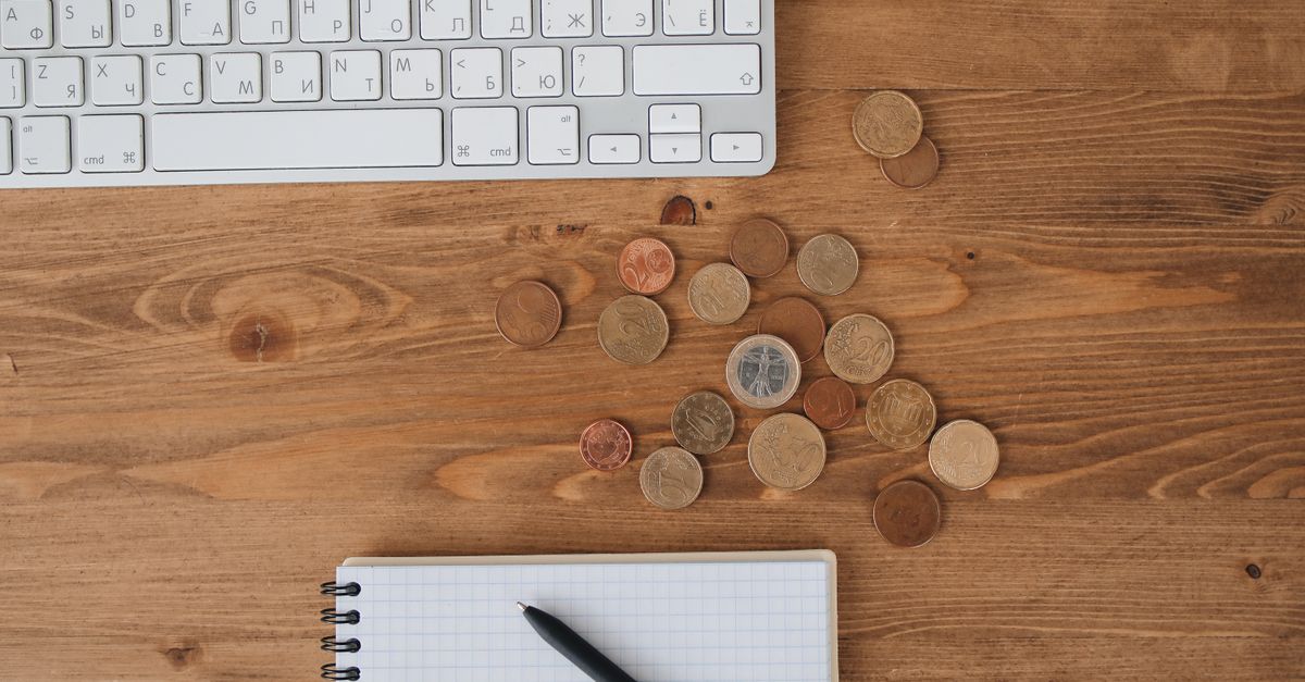 Scattered coins on a wooden desk alongside a keyboard and notebook, captured from above.