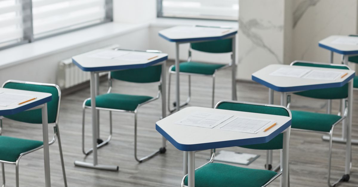 An empty classroom with arranged desks, exam papers, and pencils ready for students.